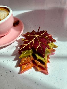 a cup of coffee and some leaves on a saucer next to a pink plate