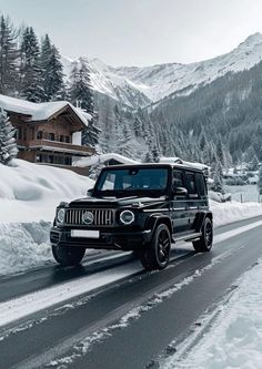 a black jeep driving down a snow covered road in front of a mountain side house