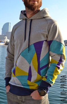 a man standing in front of the water wearing a hoodie with an abstract design on it