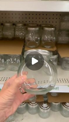 a person is holding a glass bowl in front of shelves full of jars and containers