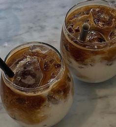 two glasses filled with ice and brown liquid on top of a marble counter next to each other