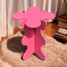 a pink table sitting on top of a shaggy rug next to a book case and window