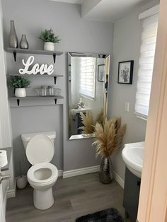 a white toilet sitting in a bathroom next to a sink under a mirror with the word love on it