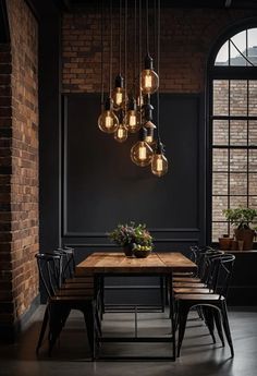 a dining room table with chairs and lights hanging from it's ceiling in front of a brick wall