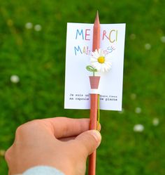 a hand holding a pencil with a flower on it and a note attached to the end