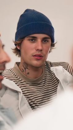 a man wearing a blue beanie and looking at another man with tattoos on his neck