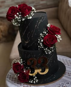 a three tiered black and gold cake with red roses on the top is decorated with white baby's breath