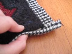 a person is holding a piece of fabric on a wooden table with a red and black checkerboard design