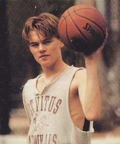 a young man holding a basketball in his right hand and wearing a tank top on the other