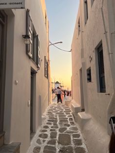 an alley way with people walking down it and buildings on either side that have shuttered windows