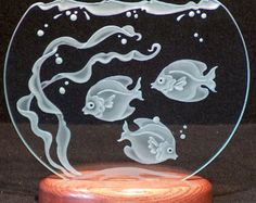 a glass plate with some fish in it on a wooden base and water bubbles coming out of the bottom