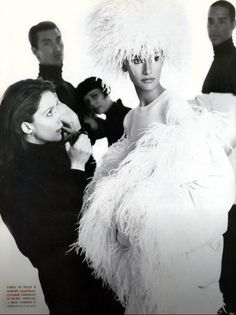 the woman is posing with two men in black and white outfits, both wearing ostrich feathers