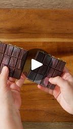 two hands are holding chocolate bars on a wooden surface