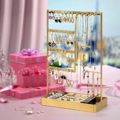 a gold jewelry stand with lots of necklaces and earrings on it next to a pink gift box