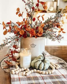 a vase filled with flowers and candles on top of a plaid table cloth next to pumpkins