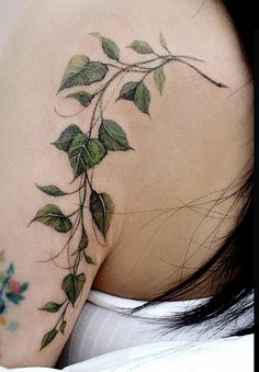 the back of a woman's shoulder with green leaves on it and flowers around her neck