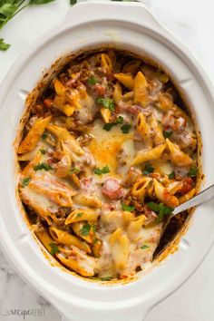 a white casserole dish filled with pasta and meat, garnished with parsley