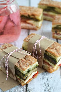 sandwiches wrapped in brown paper sitting on top of a wooden table next to a mason jar