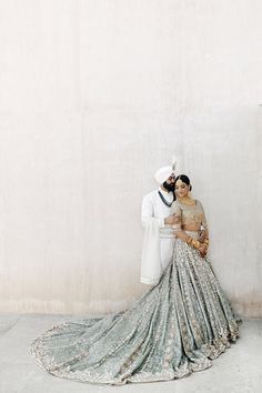 a man and woman standing next to each other in front of a wall wearing wedding outfits