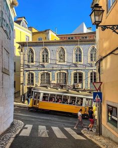 a yellow trolley is going down the street in front of some buildings and people walking by