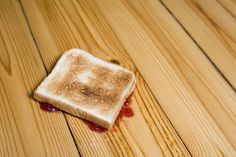 a piece of toast with jam on it sitting on top of a wooden floor that says, dj just dropped my jam