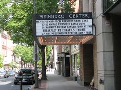 a theater marquee on the side of a street with cars parked in front