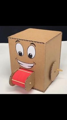 a cardboard box with a face on it and a red ribbon in its mouth, sitting on a white surface