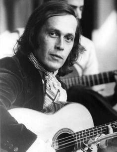 a black and white photo of a man holding an acoustic guitar in his right hand