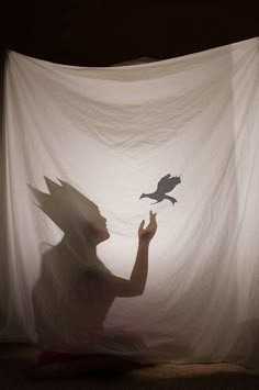 a woman is sitting in front of a curtain with a bird on her head and an animal flying through the air