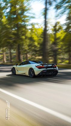 a white sports car is driving down the road in front of some trees and bushes