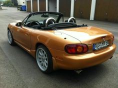 an orange sports car parked in front of a building with two doors open and the roof down