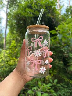 a hand holding a mason jar with pink bows and daisies on the lid, in front of some trees