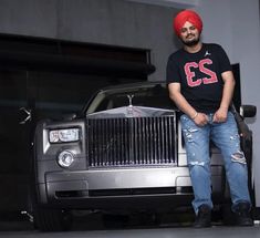 a man sitting on the hood of a car wearing a red turban and jeans