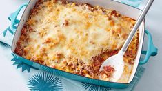 a casserole dish with meat and cheese in it on a blue napkin next to a spoon