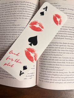 an open book with red lipstick on it and some playing cards in front of it