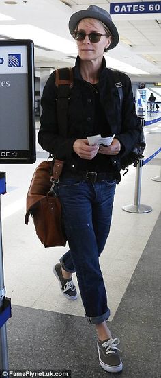 a woman in black jacket and hat walking through an airport with her hand on her hip