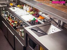 a stainless steel bar with lots of bottles and drinks on the counter, next to a sink