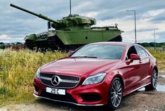 a red car parked in front of a tank