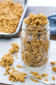 a glass jar filled with granola sitting on top of a table next to a baking pan