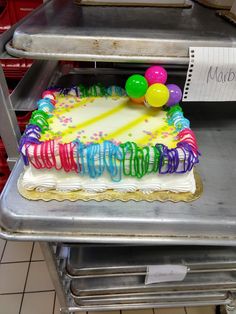 a birthday cake with colorful icing and balloons on it sitting on top of a metal tray