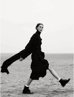 black and white photograph of woman in dress running on the beach with her legs spread out