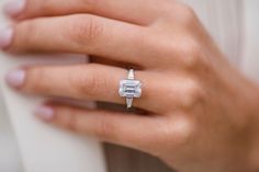 a woman's hand with a diamond ring on her left hand, wearing a white shirt