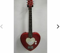 a red guitar hanging on the wall with a heart shaped pickle attached to it