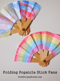 two colorful paper fans sitting on top of a white surface with text reading folding popsicle stick fans