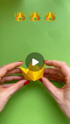 two hands are holding an origami crown and playing with the video game's screen