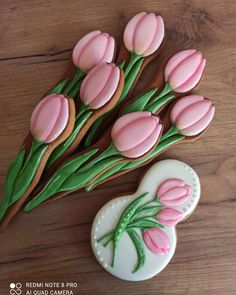 decorated cookies with pink flowers and green stems on a wooden table next to a cookie