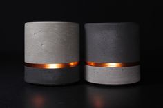 two concrete candle holders with gold rims on black background, side by side one is grey and the other is white