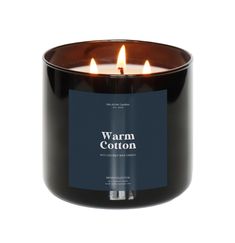 a black candle with two lit candles in it and the words warm cotton on top