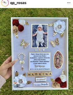 a hand holding up a framed photo with flowers and other things on it in the grass