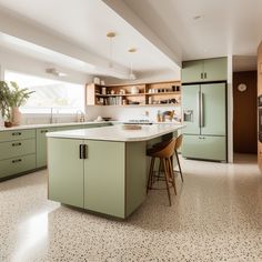 a kitchen with green cabinets and white counter tops, an island in the middle has two stools on it